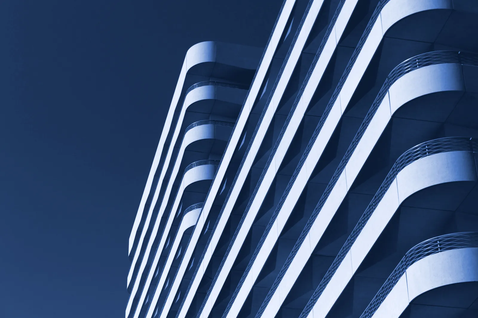 Curved white balconies of a modern building against the sky in blue duotone